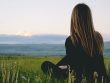 Woman enjoying peace in a lush green field with a scenic mountain view during sunset.