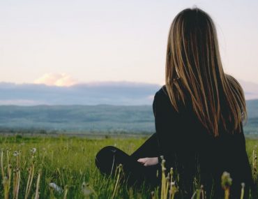 Woman enjoying peace in a lush green field with a scenic mountain view during sunset.